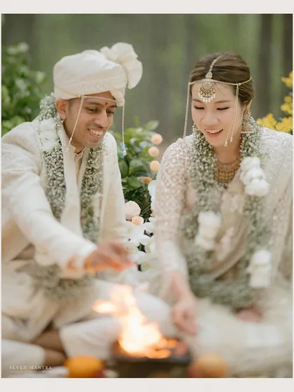 A shared smile during their wedding rites. The focus is on the couple's genuine interaction, with the natural forest setting and soft floral decor creating a peaceful and intimate atmosphere.