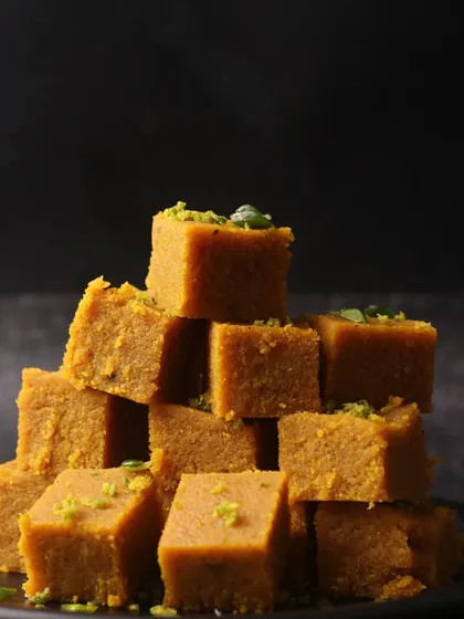 A stack of Mohanthal, a dense, gram-flour fudge. The composition creates a sense of abundance and indulgence.