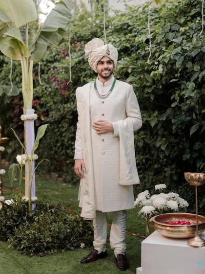 A classic portrait of the groom in his ivory sherwani, looking sharp and ready for his wedding ceremony in a lush garden setting.