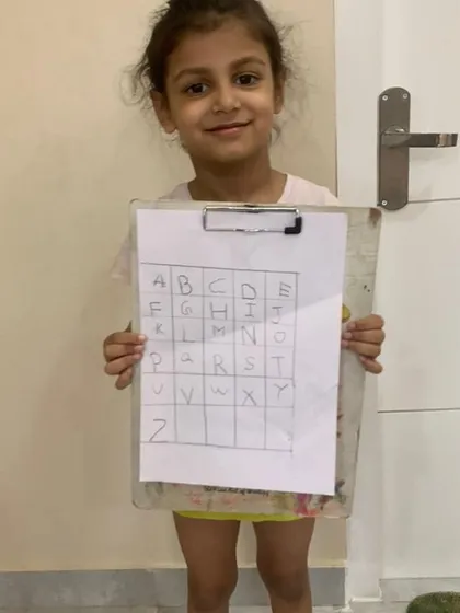 A proud student showing her completed alphabet grid. Activities like this help with letter recognition and writing practice in a structured yet simple format. Seeing her smile is the best reward.
