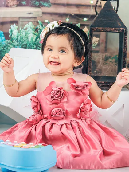 A happy baby girl in a pink dress, playing with a toy piano in a whimsical garden setting.
