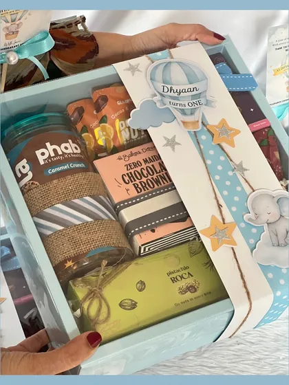 This larger return favor box includes a jar of caramel crunch, a chocolate brownie, and other goodies, all tied together with the adorable hot air balloon and elephant theme.