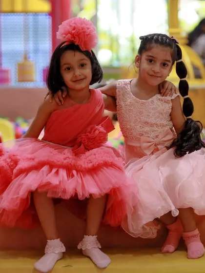 Two girls in their beautiful party dresses, posing by the ball pit during a unicorn-themed celebration.