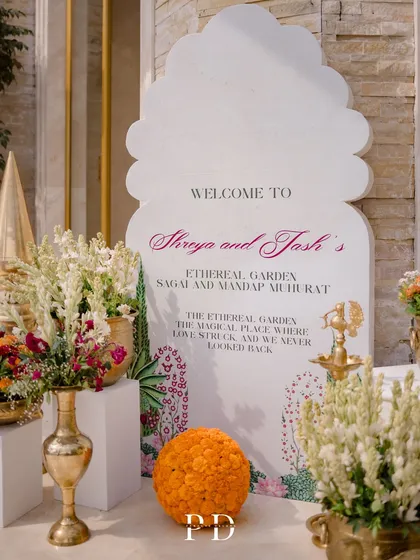 A custom-shaped welcome sign for an 'Ethereal Garden' Sagai, adorned with marigold balls and brass vases filled with tuberoses.