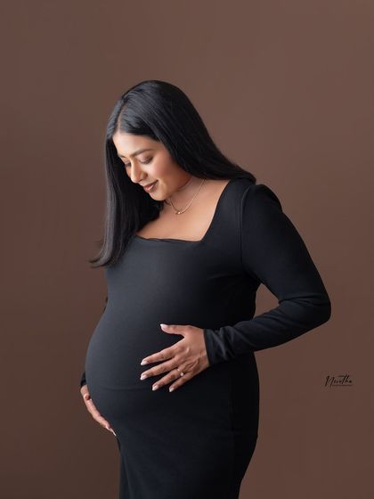 A classic studio maternity portrait of a mom-to-be in a form-fitting black dress.