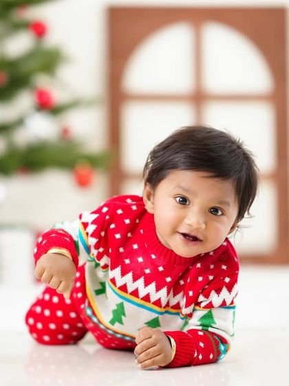 A happy baby boy crawling on the floor during his festive Christmas photoshoot, dressed in a cozy holiday sweater.