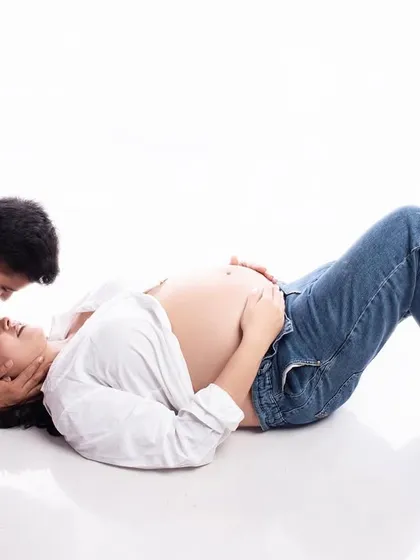 A romantic and intimate pose with the couple lying on the floor. The bare bump and casual outfits create a very personal and authentic portrait of their connection.