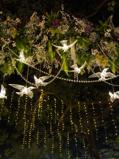 A whimsical decor detail featuring illuminated crystal birds and delicate fairy lights hanging from a floral arrangement, creating a magical, starry-night effect.