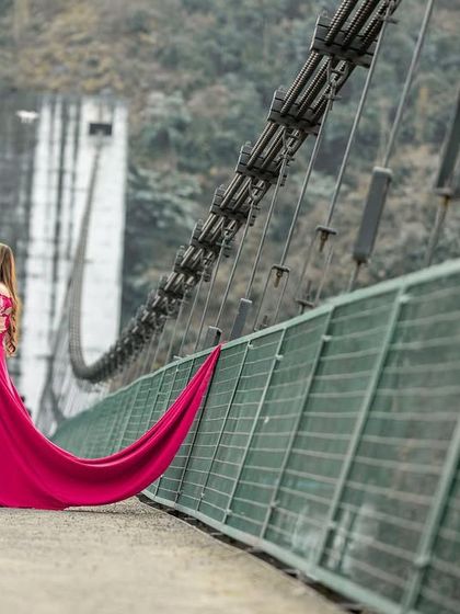 A romantic portrait of the couple on a suspension bridge, with the bride's long trail gown adding a dramatic flair to the pre-wedding photo.