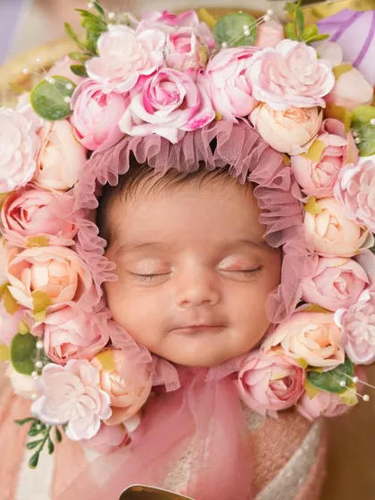 A close-up of a newborn girl wearing an elaborate pink floral bonnet. This 'blooming baby' theme is incredibly sweet and artistic.