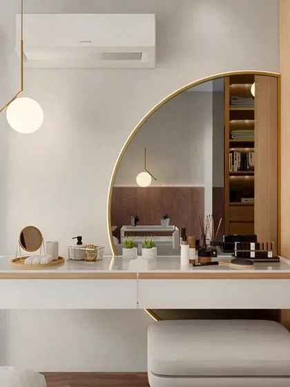 A clean and bright vanity design with a floating white counter and a large, organically shaped mirror. The simple pendant light and wood-paneled wardrobe add warmth and style to the space.