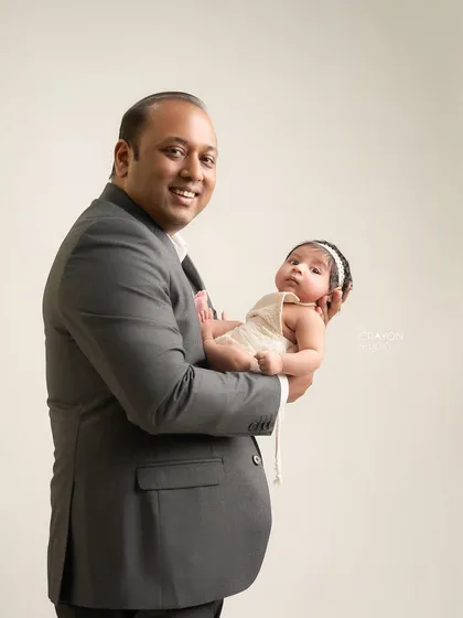 A proud father holds his newborn, smiling at the camera. This image captures the joy and pride of fatherhood in a classic, clean studio setting.