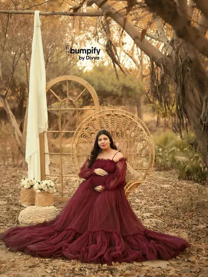A solo portrait of the mom-to-be seated on the wicker peacock chair. The earthy tones of the background and her dress create a warm and inviting atmosphere.