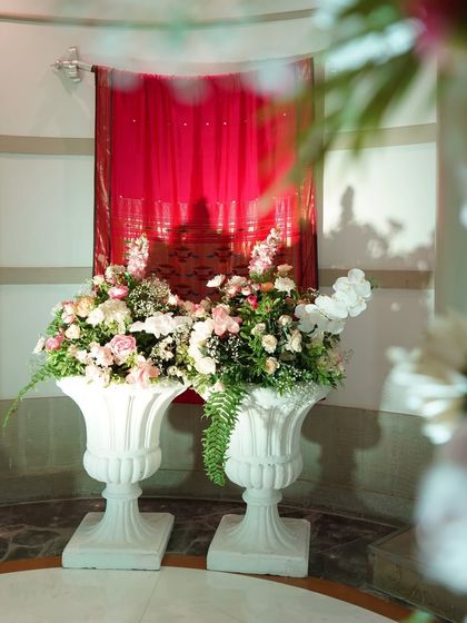 Classic white urns filled with pink and white floral arrangements stand against a rich red curtain, creating a beautiful color contrast and adding a touch of elegance to the space.