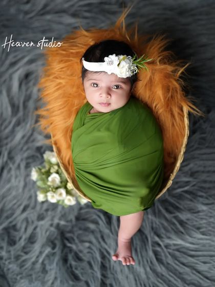 A beautiful portrait of a newborn girl, swaddled in olive green and wearing a delicate floral headband. Her direct gaze makes for a captivating and precious memory.