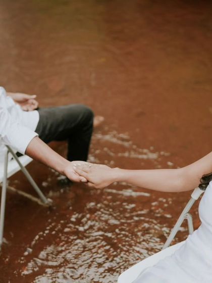 An artistic and symbolic shot of a couple holding hands while seated in chairs surrounded by water. This conceptual photo is about connection and trust.