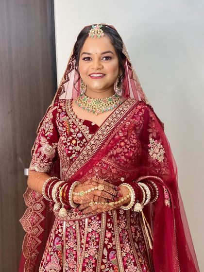 A full-length photo of the bride in her red lehenga. The hairstyle is elegant and complements the heavy embroidery of her outfit.