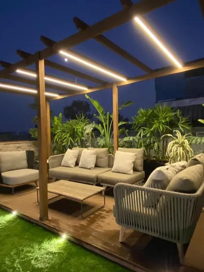 A perfect example of a modern terrace designed for real life. This setup features a custom wooden pergola with integrated LED lighting, comfortable all-weather furniture, and a backdrop of tropical plants, creating an ideal space for hosting or relaxing.