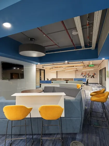 A collaboration zone with a mix of sofa seating and high-top chairs. The blue and yellow color scheme is energetic and youthful.