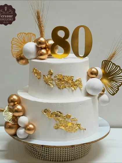 Celebrating a big milestone like an 80th birthday calls for a grand cake. This two-tier eggless cake features a sophisticated white and gold design with delicate gold leaf, spheres, and custom toppers, all based on a picture the client shared.
