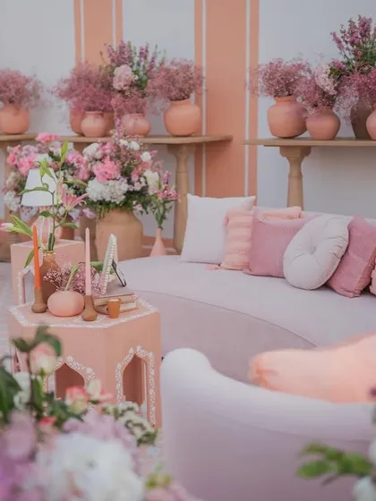 A plush, curved sofa in soft pink is surrounded by florals, creating a luxurious and comfortable lounge space for guests at the 'Handpainted Story' wedding.