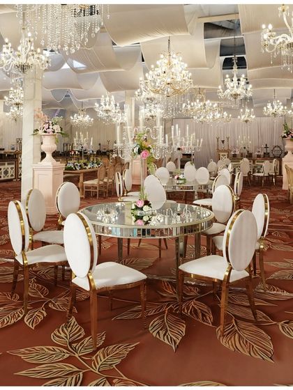 A close-up of the luxurious table setting. The mirrored table, elegant white and gold chairs, and dozens of crystal chandeliers create a dazzling and opulent dining experience.