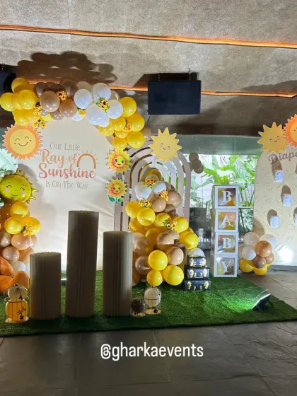 A full view of the "Our Little Ray of Sunshine is on the way" baby shower theme. The setup includes a teddy bear, a sunshine-themed backdrop, and a cheerful yellow and brown balloon arch.
