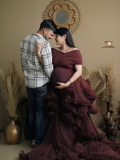 An intimate pose showing the couple's connection. They stand forehead-to-forehead, wrapped in an embrace, with the flowing maroon gown adding a touch of romance to this studio shot.
