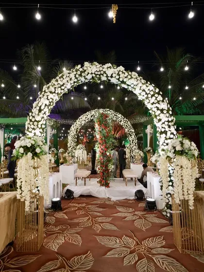 An elegant evening reception under the stars. The series of white floral arches creates a dreamy, romantic pathway, while the warm lighting adds a touch of magic, proving that luxury is a feeling, not just a look.