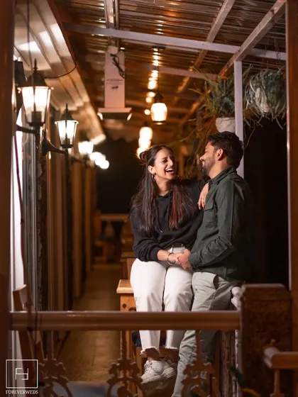 A relaxed evening moment on a beautifully lit verandah. The warm string lights create a cozy and inviting atmosphere for Ishu and Arihant's shared laughter, showing that romantic shots can also be casual and comfortable.