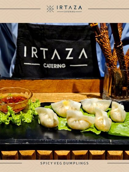 Spicy Veg Dumplings presented on a sleek black platter with our signature Irtaza apron in the background. A perfect bite-sized appetizer packed with flavor.