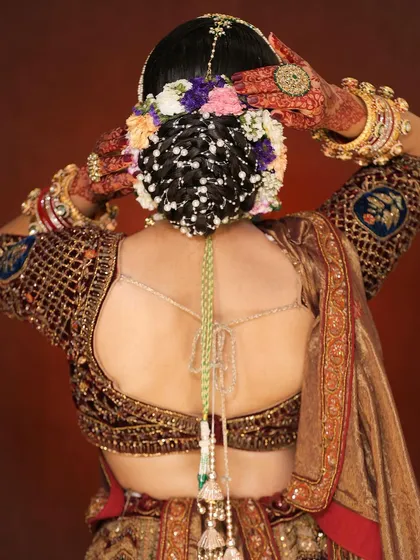 A back view of a classic bridal updo. The bun is intricately woven and adorned with a mix of colorful flowers and delicate pearl strings, showcasing our attention to detail.