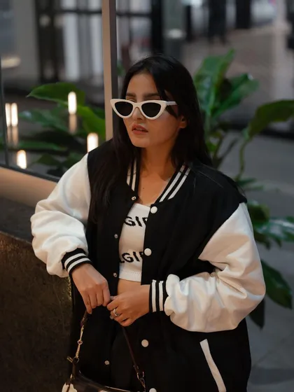 A stylish portrait of a model in a varsity jacket, leaning against a window. The reflection and the indoor plants add layers to this cool, urban shot.