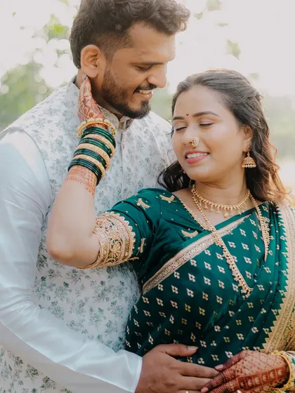 A tender moment captured in a sunlit field. The groom's gentle touch and the bride's happy expression show their deep comfort and affection. The traditional green saree looks beautiful in the soft morning light.
