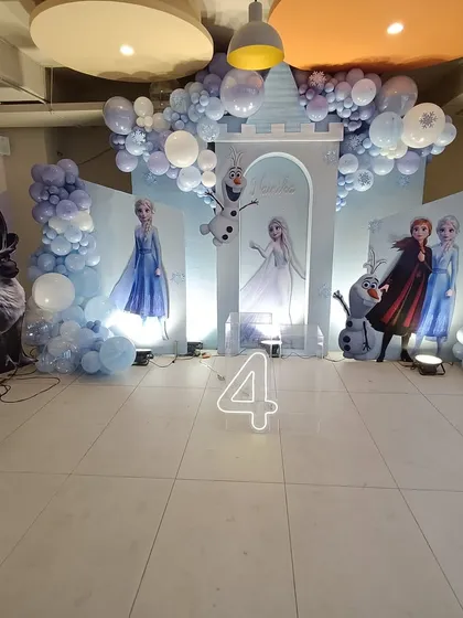 The full stage for a Frozen-themed fourth birthday party. The setup includes a light-up number '4', all the main characters, and a balloon arrangement that looks like falling snow, creating a complete winter wonderland.
