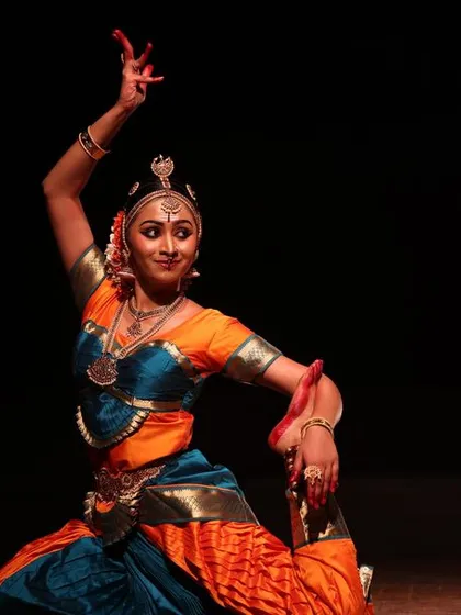 A solo dancer in a graceful, seated pose, her movement telling a story, captured at the Sadhana Classical Dance Festival.