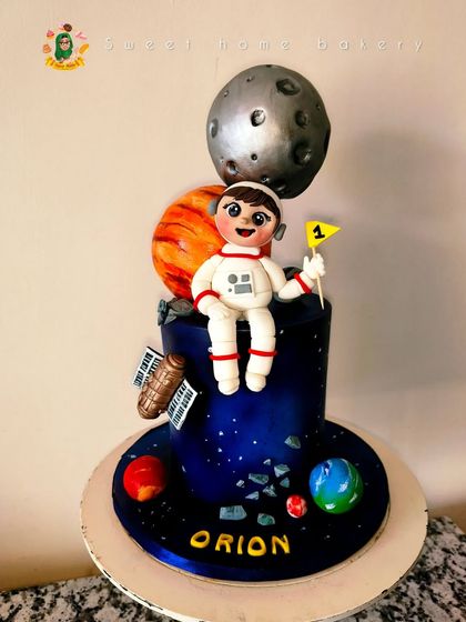 A cake that's truly out of this world for a little astronaut named Orion. This space-themed design features a deep blue galaxy, a custom astronaut figurine, and edible planets like a textured moon and Jupiter. It’s a perfect cake for a first birthday adventure.