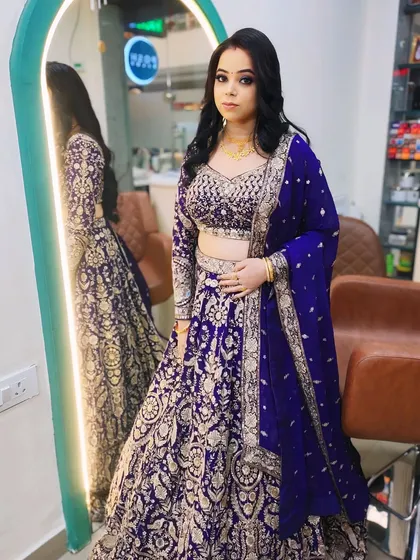A full-length shot of a client ready for a wedding party. Her royal blue and silver lehenga is complemented by a bold eye and a soft wavy hairstyle.