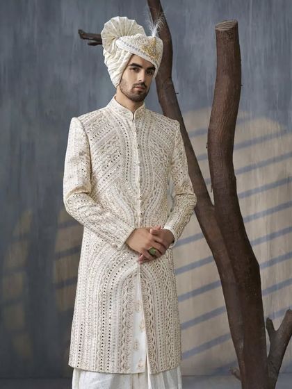 A groom stands poised in an off-white sherwani, featuring intricate self-colored embroidery. The matching safa and the subtle elegance of the outfit make it a timeless choice for a day wedding.