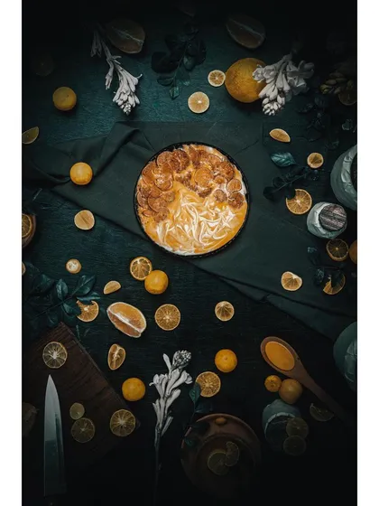 An artistic flat lay of a lemon tart, using a dark and moody theme to create a visually rich, textured image. This style of food photography is ideal for social media content, cookbooks, and brand storytelling.