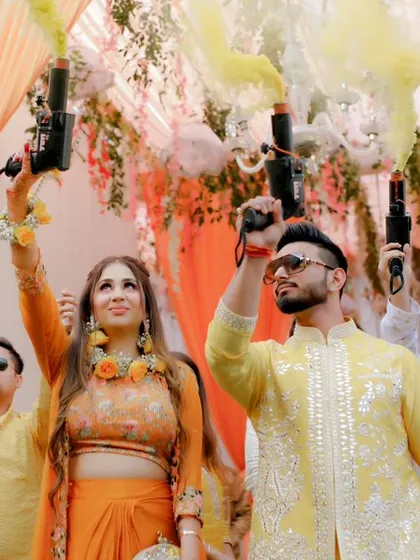 Akhilesh and Nisha make a grand entrance at their Haldi ceremony, surrounded by friends and colorful smoke bombs, ready for a day of fun.