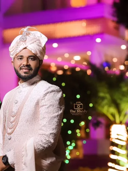 A handsome groom posing at his wedding venue. The green lights in the background add a nice contrast to his white sherwani.