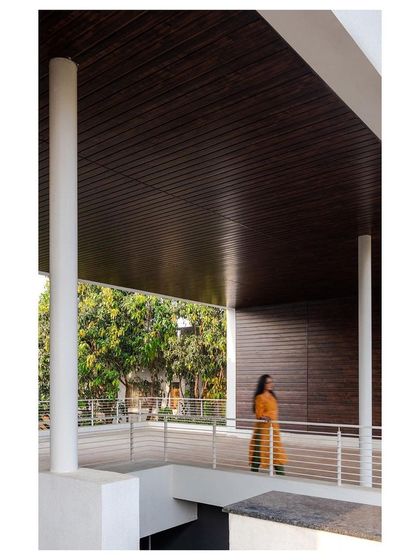 A covered walkway on the upper level of the "Solid | Void | Solid House" overlooks the garden below. The dark wood ceiling contrasts with the white columns, creating a rhythmic and sheltered passage.