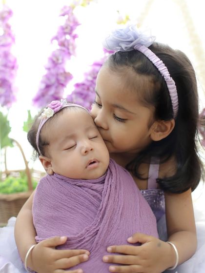 A tender kiss from a big sister to her new baby sibling. The coordinating purple outfits and floral background make this newborn and sibling portrait extra special.