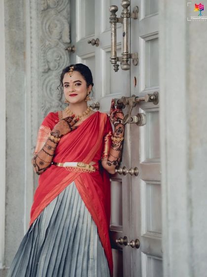 An elegant portrait of the bride standing by a traditional door. Her red and grey half saree and intricate henna are beautifully showcased in this shot.