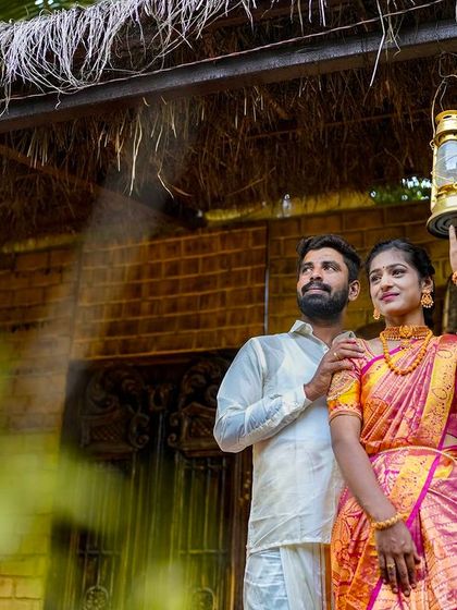A couple poses in front of a rustic hut with hanging lanterns, perfect for a village-themed or traditional shoot.