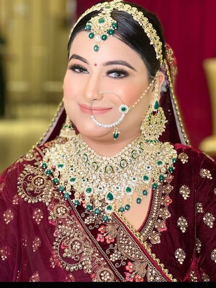 A classic bridal portrait of a bride in a maroon velvet lehenga with heavy green and white kundan jewellery. The makeup is flawless and regal.