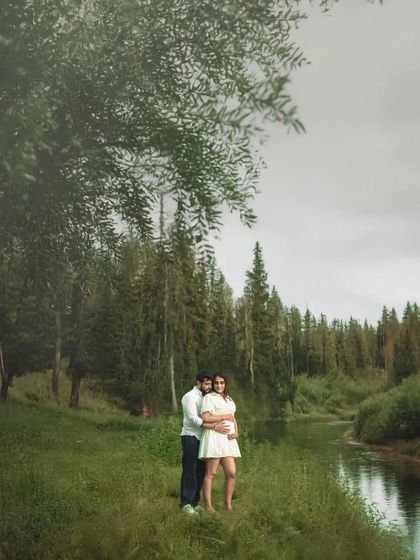 A quiet embrace by the water's edge. This image captures a serene and intimate moment, with the couple framed by the lush greenery of the forest.