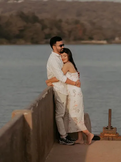 A tender hug from behind as a couple enjoys the view from a lakeside pier, capturing their closeness and affection.