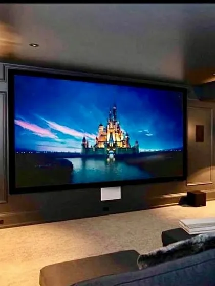 An example of a clean and elegant home cinema design. The massive, acoustically transparent screen conceals the front channel speakers, creating a seamless look. This setup, featuring sophisticated wall paneling and a plush sectional sofa, is perfect for a refined, high-performance entertainment space.